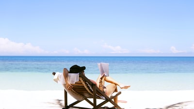 The woman sat on a brown wooden beach chair
